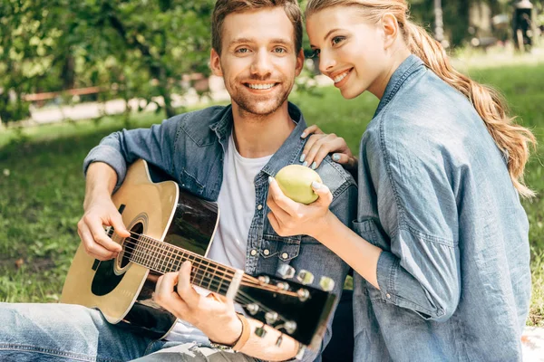 Gülümseyen Kız Arkadaşı Için Gitar Çalmak Parkta Piknik Yaparken Kameraya — Ücretsiz Stok Fotoğraf