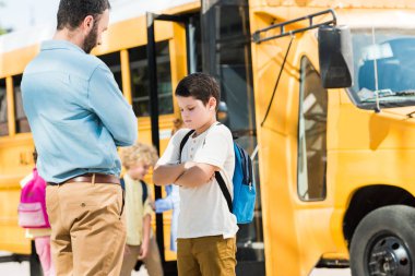 father preaching his son in front of school bus clipart