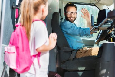 smiling bus driver greeting schoolgirl who entering bus clipart