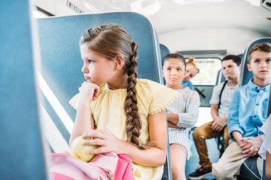 sad little schoolgirl riding on school bus with her classmates clipart