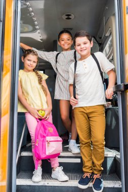 group of smiling schoolchildren standing at school bus clipart