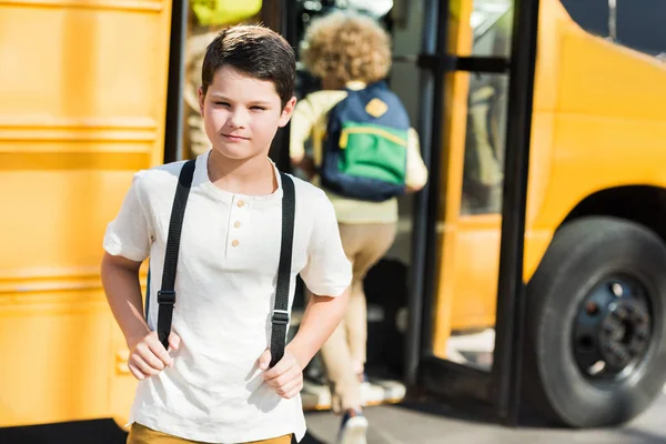 学校のバスの前でカメラを見て深刻な小さな男子生徒 — ストック写真