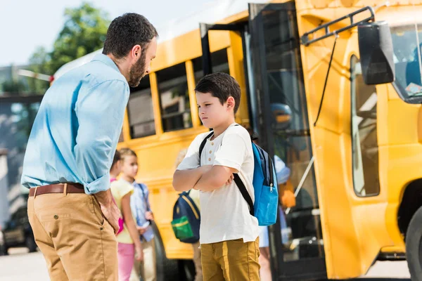 angry father preaching his son in front of school bus