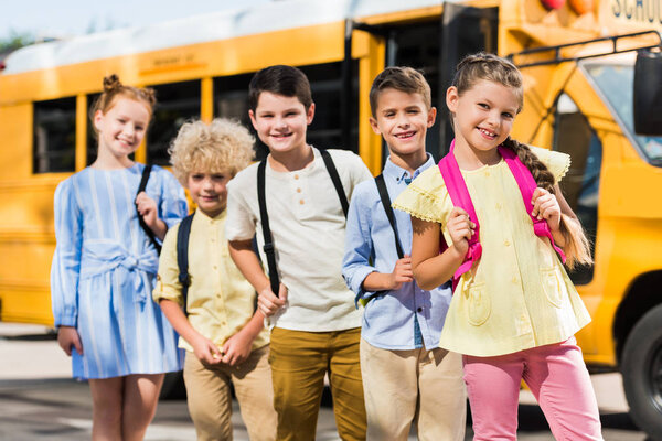 group of happy schoolchildren looking at camera in front of school bus