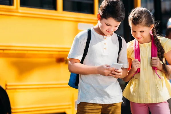 Adoráveis Pequenos Estudiosos Usando Smartphone Juntos Frente Ônibus Escolar — Fotografia de Stock