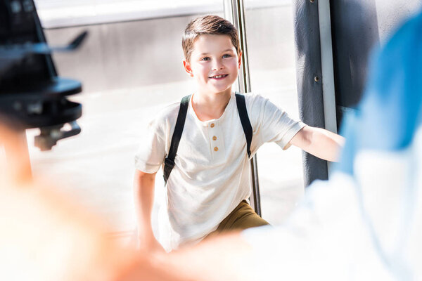 smiling schoolboy entering school bus and looking at driver