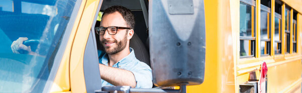 panoramic shot of handsome school bus driver smiling and driving