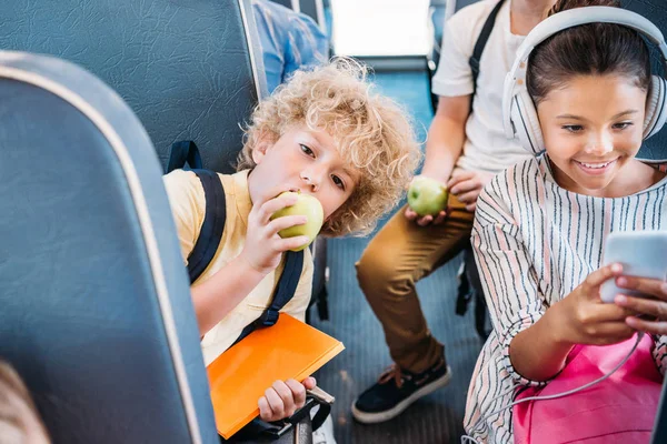 Adorable Little Apple Jedzenia Uczniak Podczas Jazdy Autobus Szkolny Kolegami — Zdjęcie stockowe