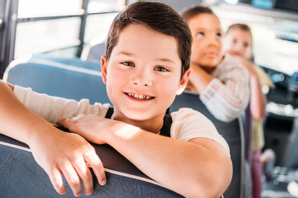 特写肖像微笑的小男孩骑在校车与模糊的同学在后台 — 图库照片