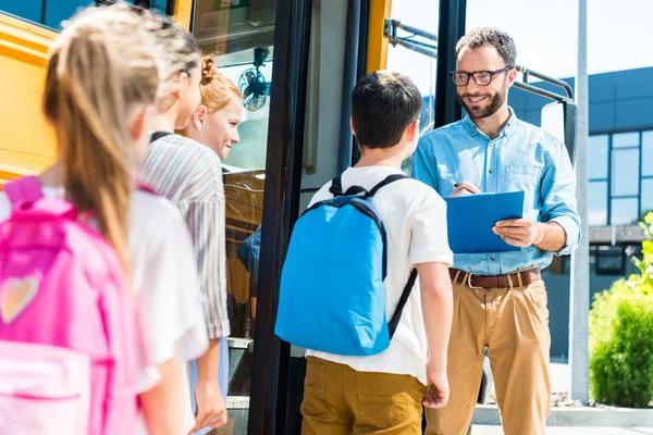 Schüler Steigen Schulbus Während Lehrer Klemmbrett Schreibt — Stockfoto