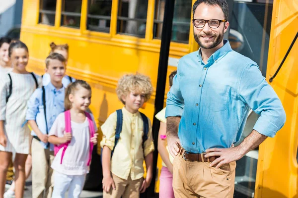 Handsome Male Teacher Looking Camera While Pupils Entering School Bus Stock Image