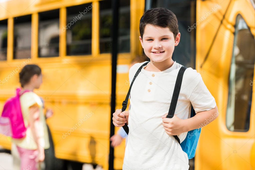 happy little schoolboy with backpack standing in front of school bus