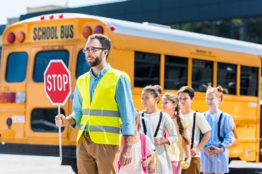 traffic guard crossing road with schoolchildren in front of school bus clipart