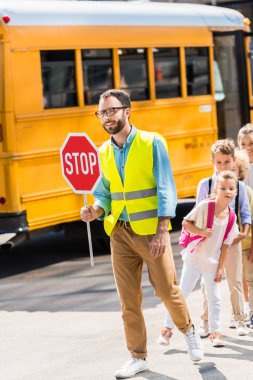 happy traffic guard crossing road with pupils in front of school bus clipart