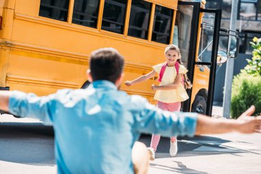 father with open arms waiting for daughter while she running from school bus clipart