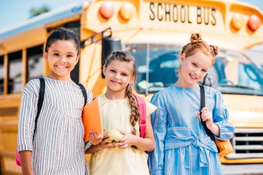 happy little schoolgirls looking at camera in front of school bus clipart