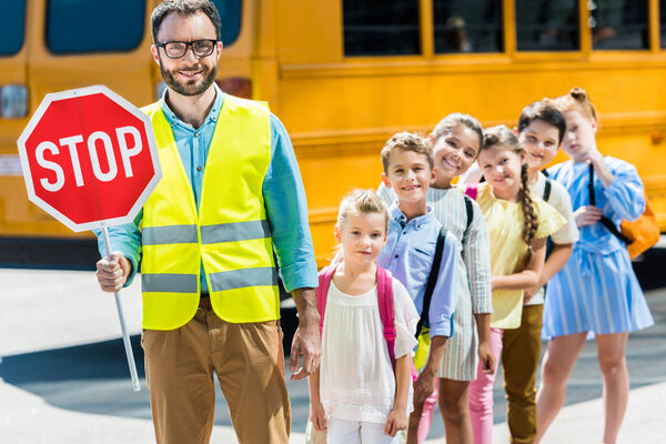 Miling traffic guard with scholars looking at camera in front of school bus

