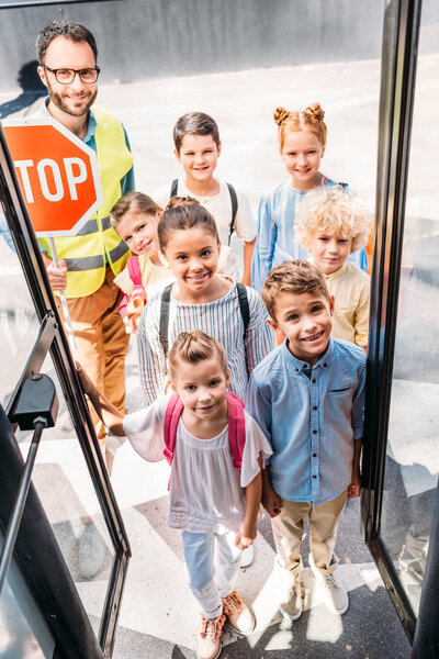 view from school bus at group of happy choolchildren with traffic guard looking at camera