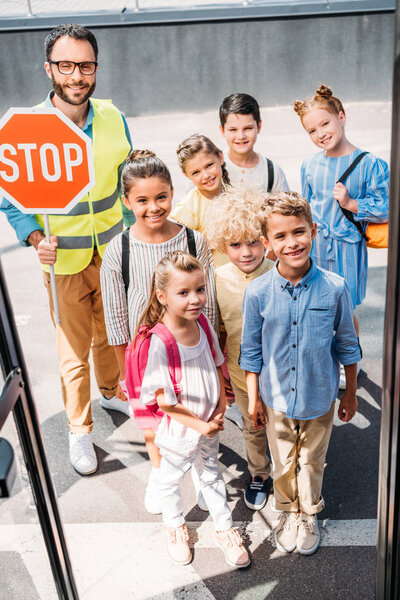 вид из школьного автобуса на группу школьников с охранником дорожного движения, смотрящим в камеру
