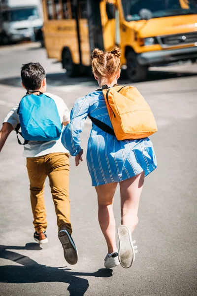 rear view of pupils with backpacks running to school bus