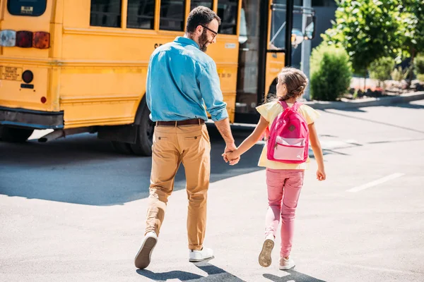 父と娘の手を繋いでいると学校のバスに歩いての背面図 — ストック写真