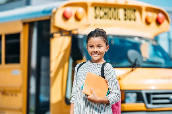 Щаслива Маленька Школярка Блокнотами Дивлячись Камеру Перед Шкільним Автобусом — стокове фото