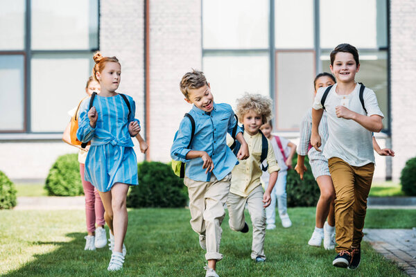 группа счастливых учащихся, бегающих по школьному саду
