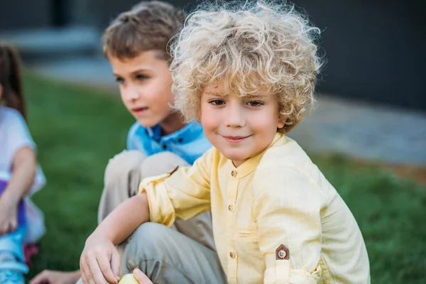 Entzückender Lockiger Schuljunge Der Mit Klassenkamerad Auf Gras Sitzt — Stockfoto