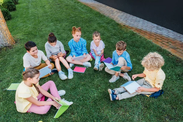 high angle view of group of pupils sitting on grass with books and devices