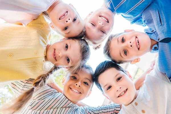 bottom biew of group of happy schoolchildren standing in circle and looking at camera