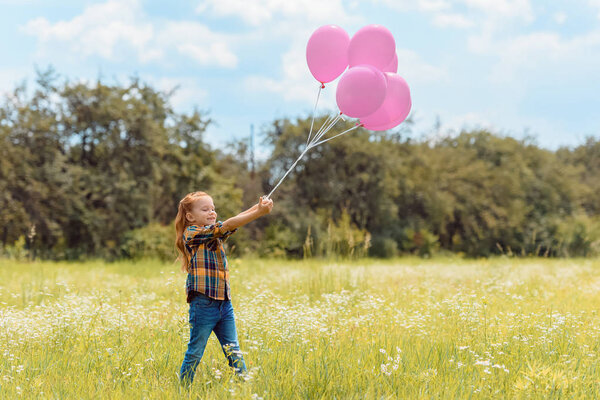 adorable child with pink balloons standing in summer field