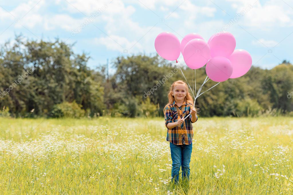 smiling child with pink balloons standing in summer field