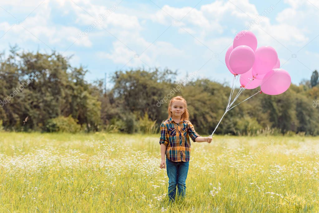 adorable child with pink balloons standing in summer field