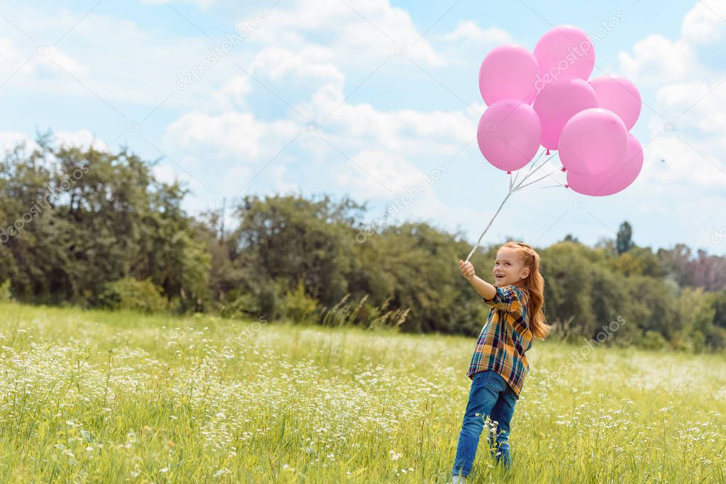 adorable child with pink balloons standing in summer field with blue sky on background