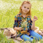 Criança sorridente com buquê de flores silvestres descansando no prado