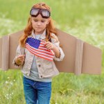 Porträt eines Kindes im Pilotenkostüm mit amerikanischem Fahnenmast auf einer Wiese