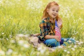 emotional kid with american flagpole resting on green grass in field