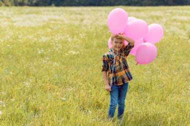yaz alanında duran pembe balonlu mutlu çocuk