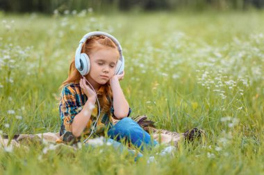 gözler küçük bir çocukla kulaklık müzik dinleme üzerinde çayır battaniyeye dinlenme sırasında kapalı