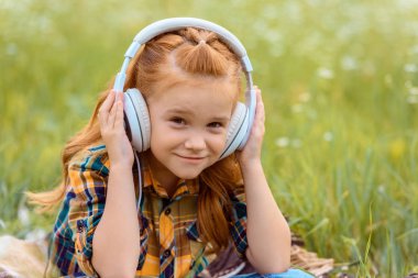 Çocuk kulaklık yeşil çimenlerin üzerinde arka plan ile müzik dinleme gülümseyen portresi