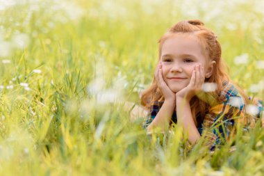 portrait of little smiling child resting on green grass in meadow clipart