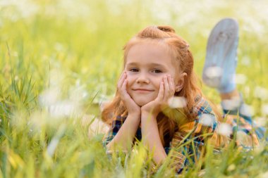 portrait of little smiling child resting on green grass in meadow