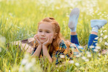 portrait of little pensive child resting on green grass in meadow