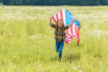 cheerful child running in field with american flag in hands clipart