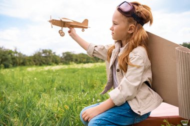 El alanındaki retro çanta üzerinde oturan ahşap oyuncak uçak pilot kostümü çocuk