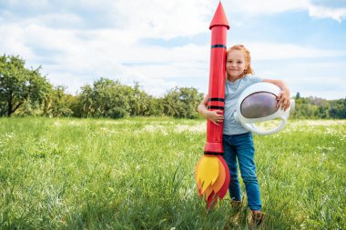 roket ve astronot kask ayakta yaz alanında olan kızıl saçlı çocuk gülümseyen