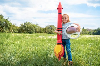 roket ve astronot kask ayakta yaz alanında olan kızıl saçlı çocuk gülümseyen