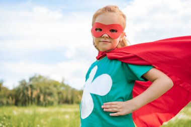 yaz çayır akimbo duran kırmızı süper kahraman kostümü içinde küçük çocuk portresi