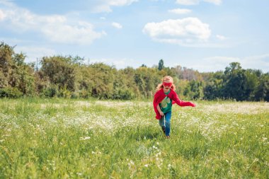little kid in red superhero costume running in meadow on summer day