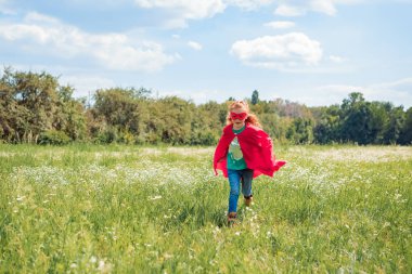 kırmızı süper kahraman pelerin ve çayır yaz gününde çalışan maskesi küçük çocuk